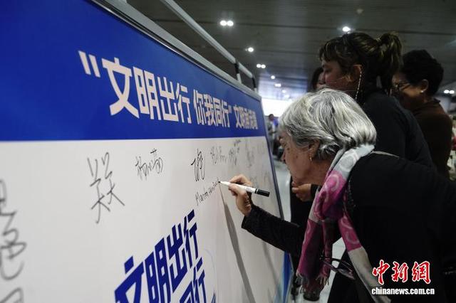 图为安阳东站，外国旅客在文明出行承诺墙上签字。翟斌 摄